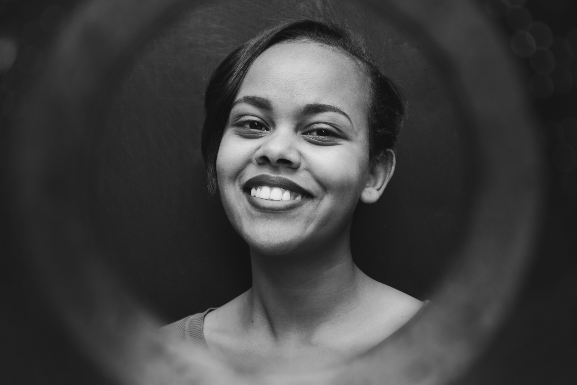 Portrait noir et blanc d'une femme avec un sourire chaleureux, encadré d'un flou circulaire