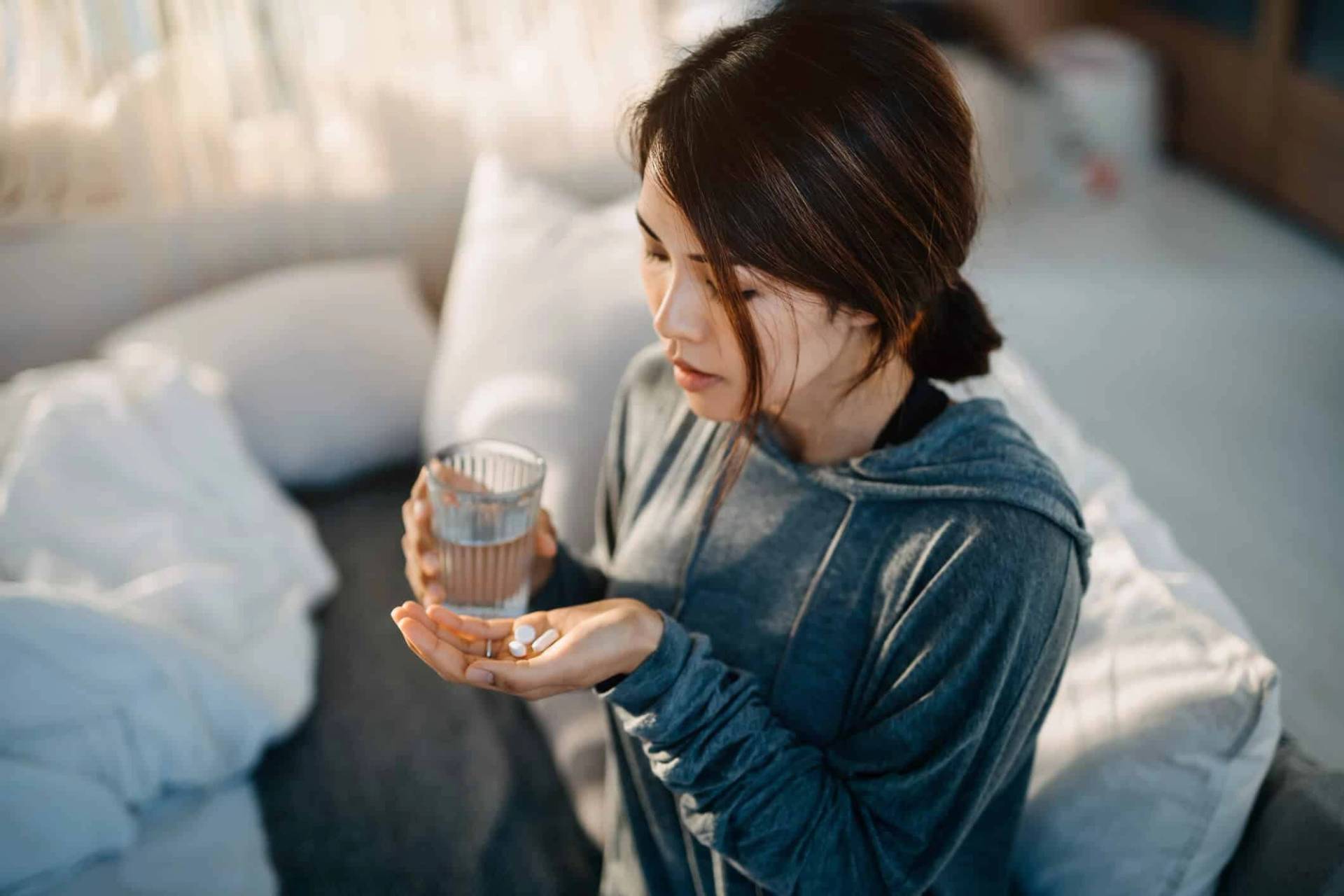 Personne tenant des comprimés et un verre d’eau dans une chambre.