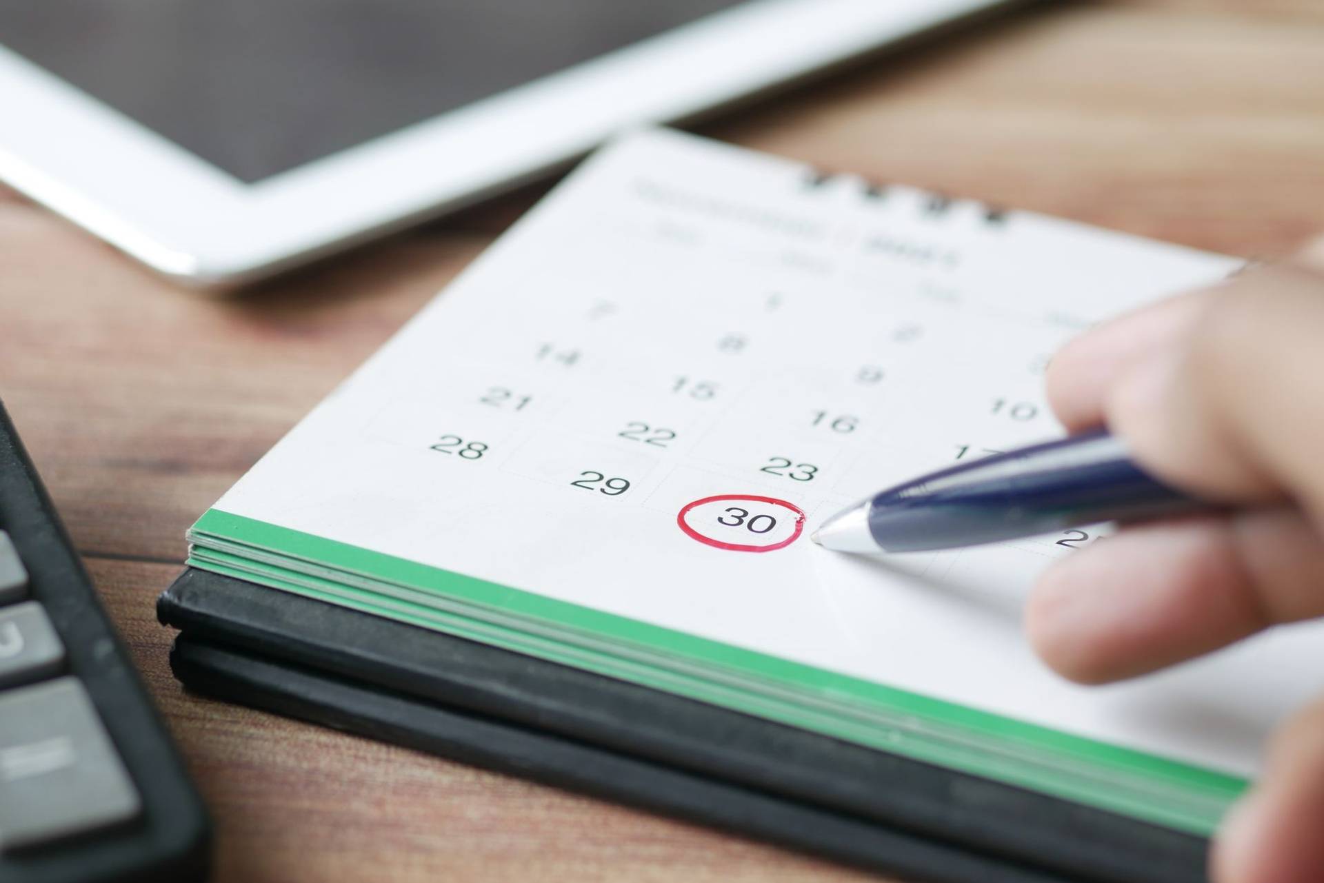 Main entourant une date sur un calendrier avec un stylo.
