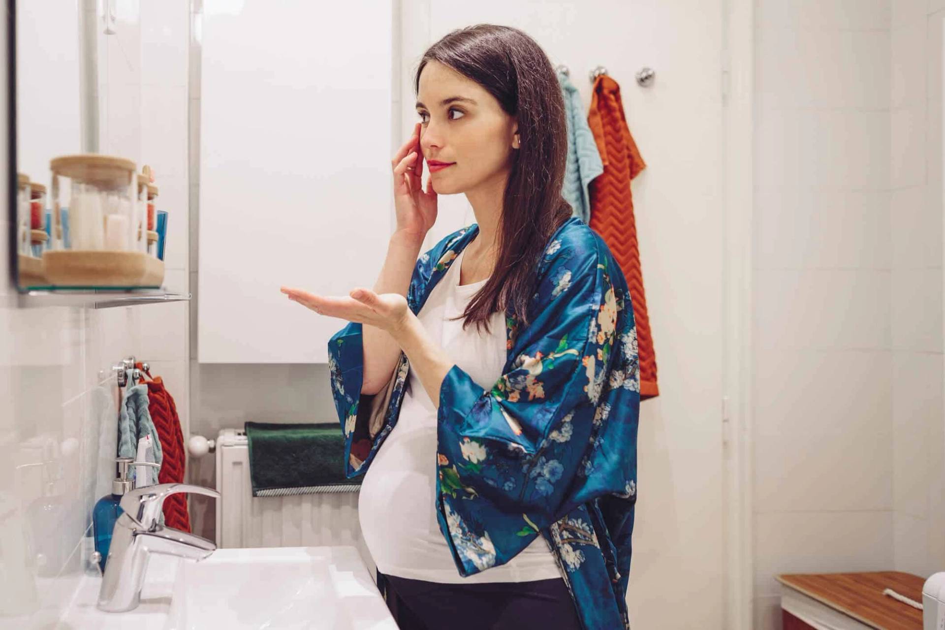 Femme au ventre arrondi examinant sa peau devant un miroir.