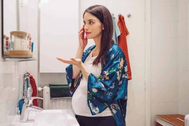 Femme au ventre arrondi examinant sa peau devant un miroir.