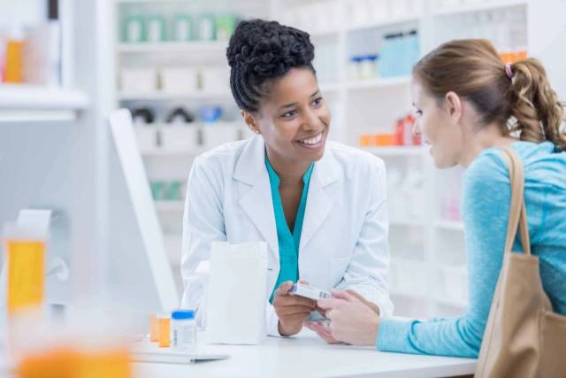 Femme échangeant avec une professionnelle au comptoir d’une pharmacie.