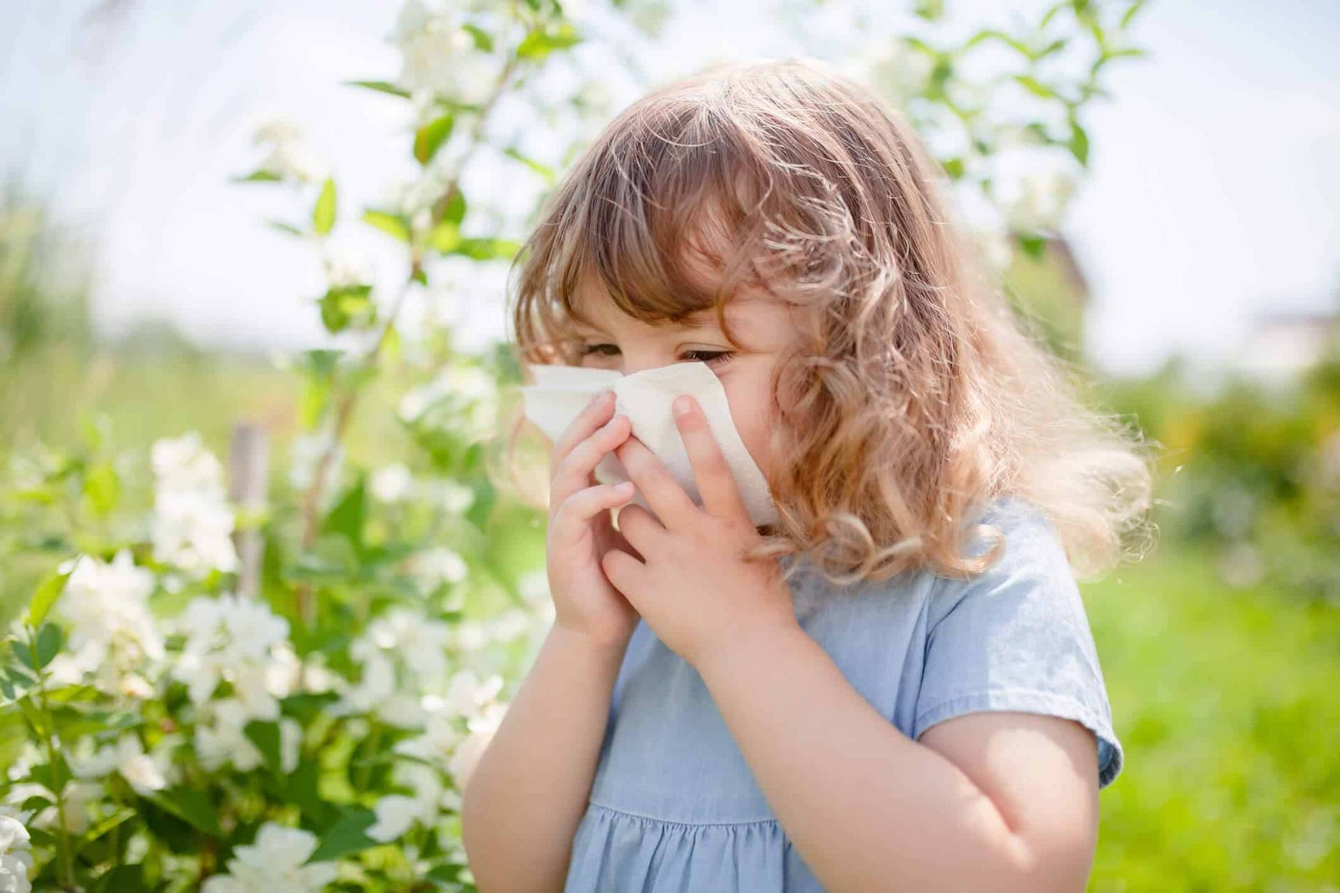Enfant se mouchant près de fleurs à l’extérieur.
