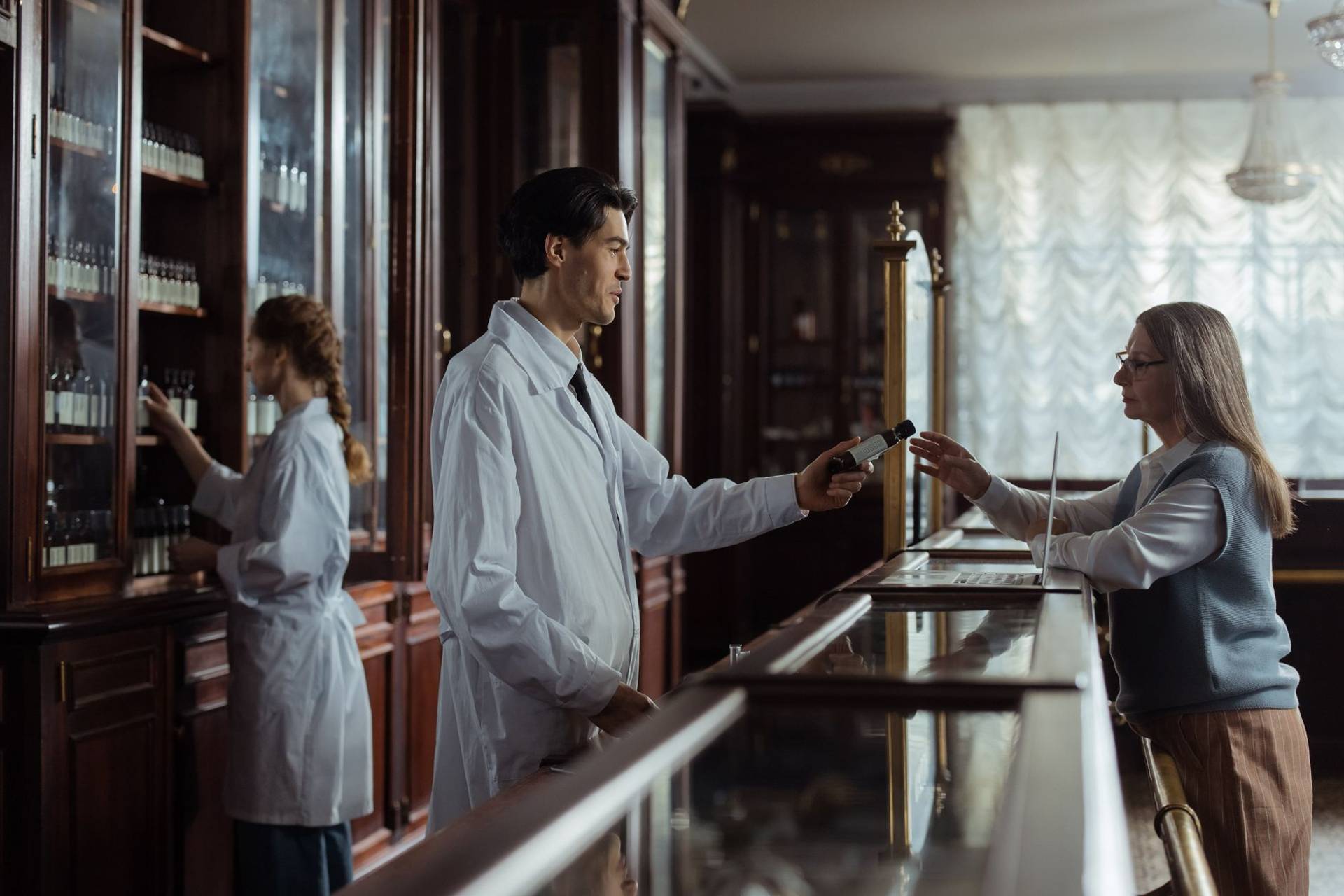 Un pharmacien remet un médicament à une cliente au comptoir d’une pharmacie.