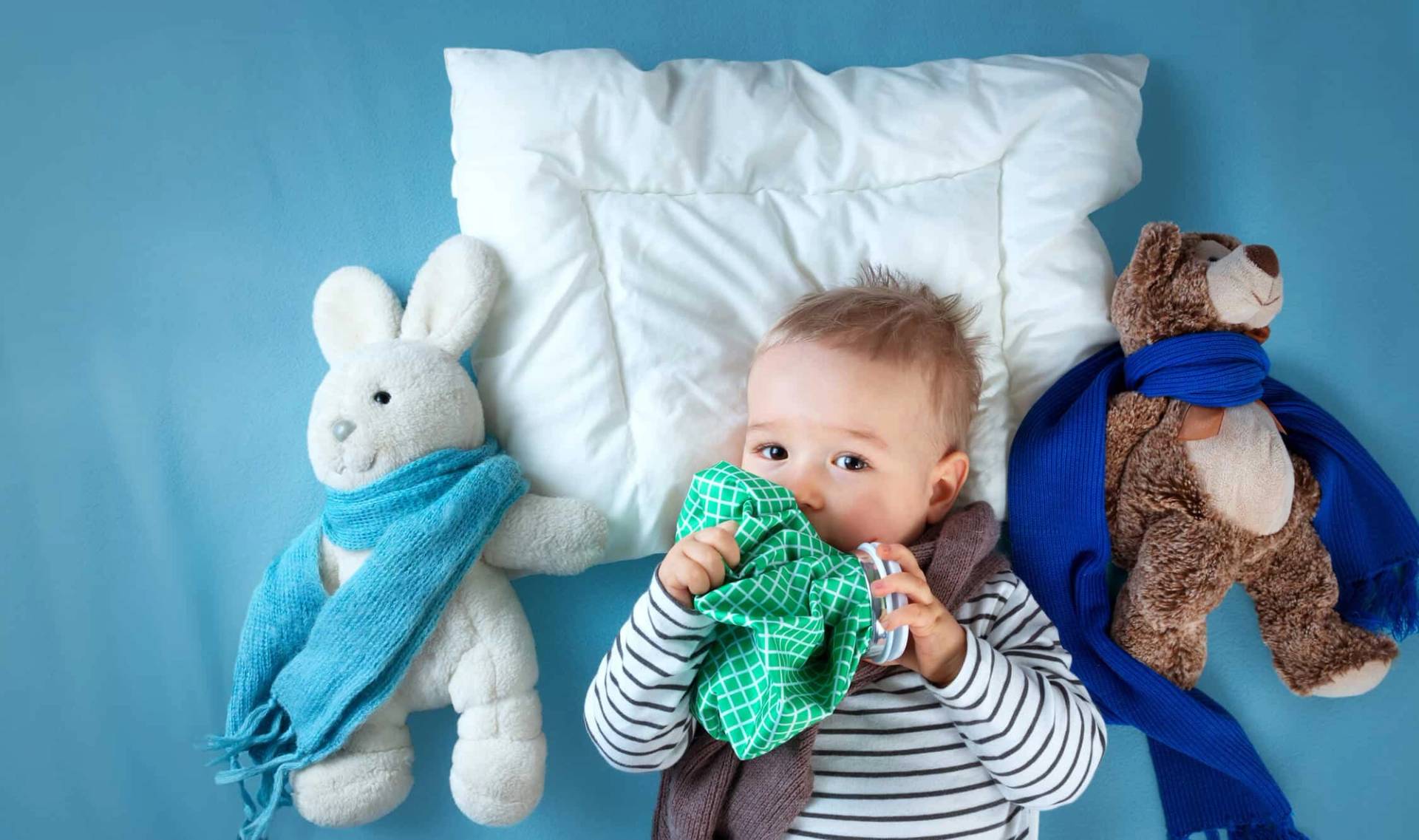 Nourrisson allongé parmi des coussins et des peluches.