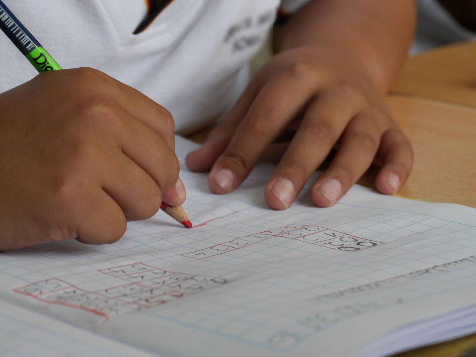 Mains d’un enfant écrivant dans un cahier avec un crayon.