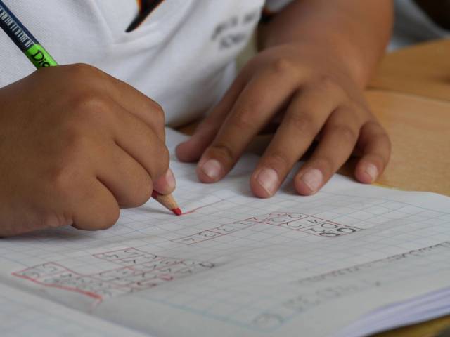 Mains d’un enfant écrivant dans un cahier avec un crayon.