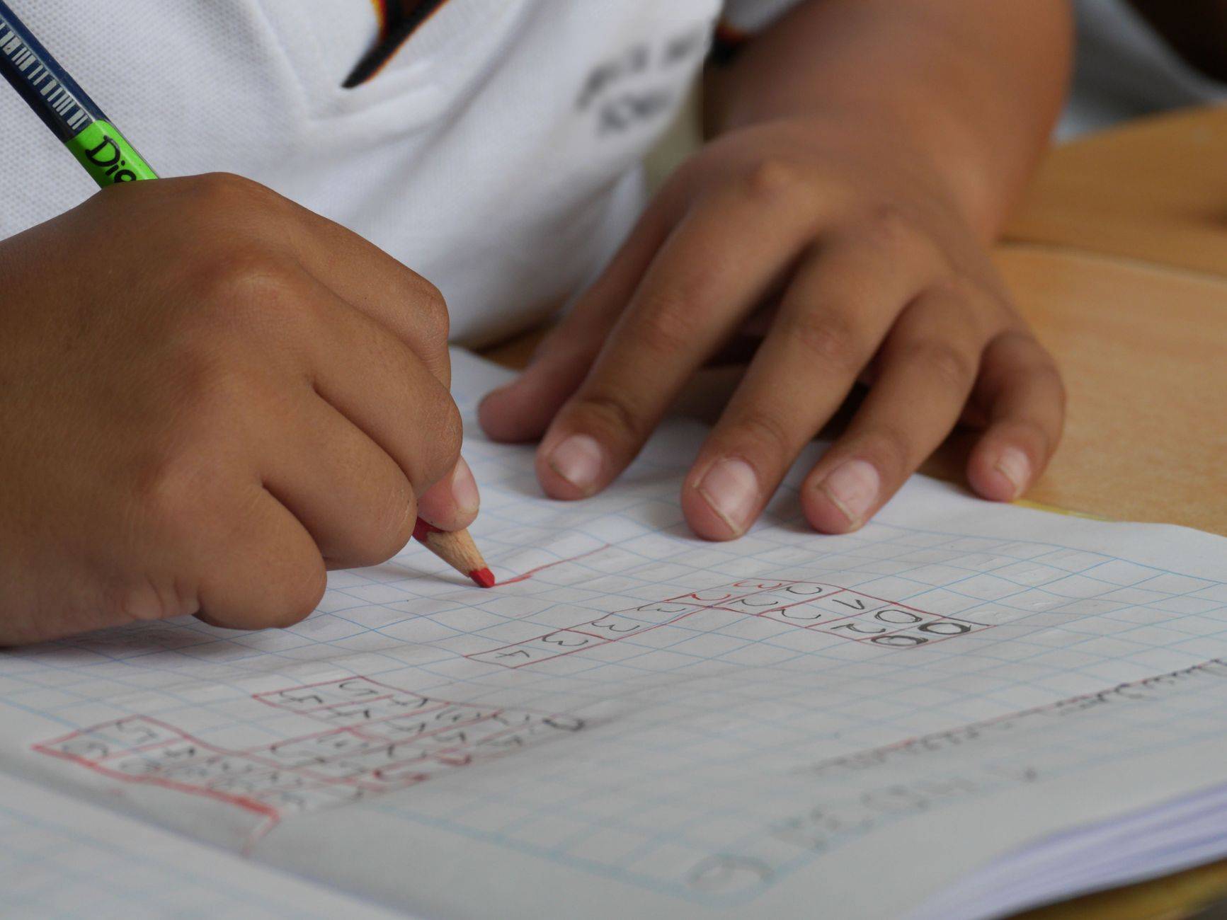 Mains d’un enfant écrivant dans un cahier avec un crayon.