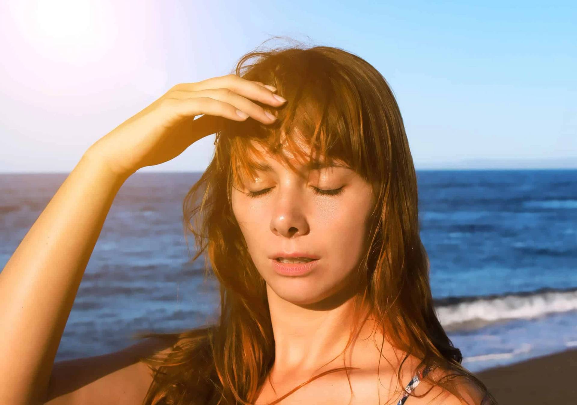 Femme tenant son front au soleil au bord de la mer.