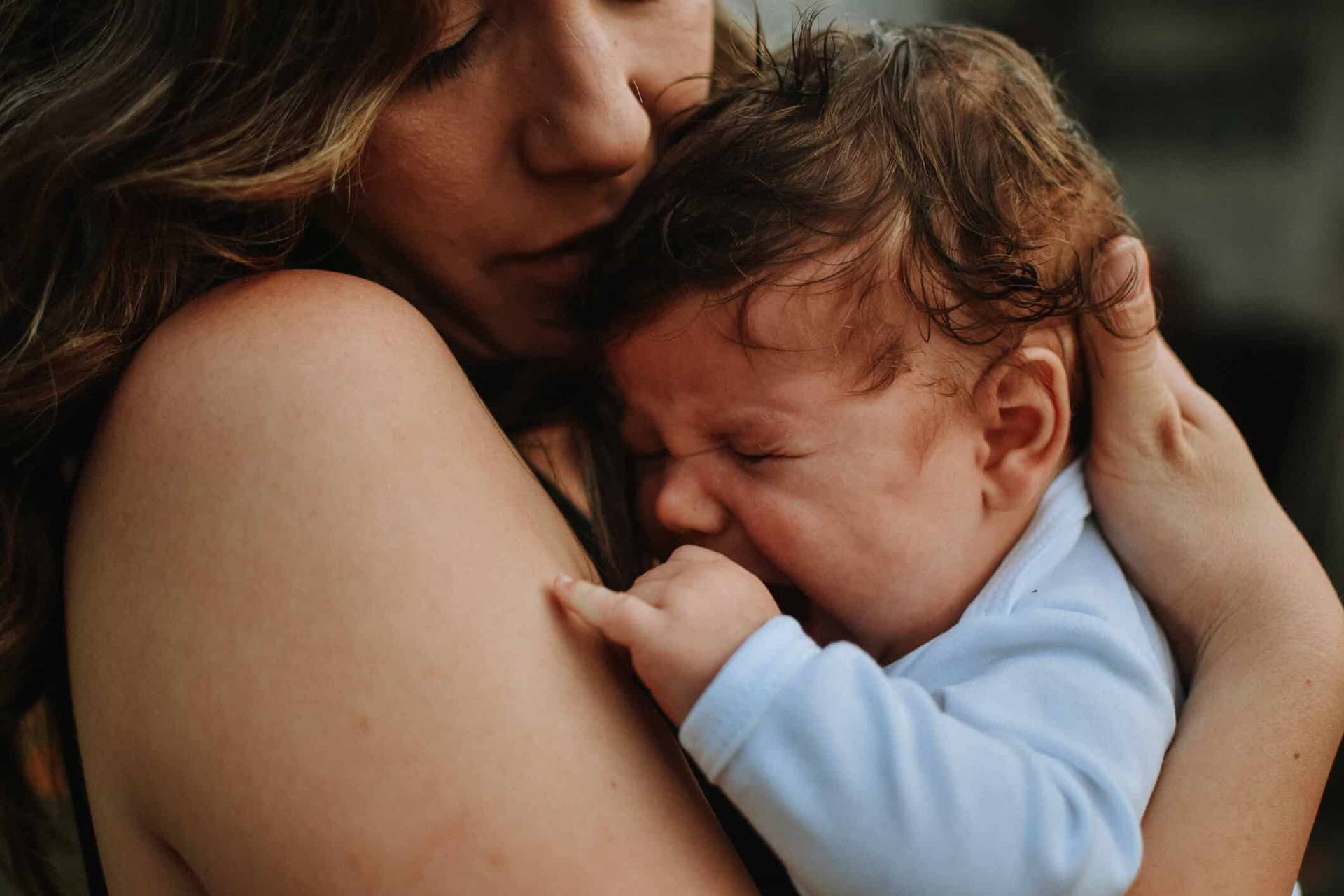 Adulte tenant un bébé qui pleure contre son épaule.