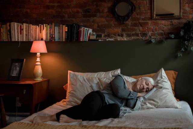 Personne allongée dans un lit dans une chambre faiblement éclairée.