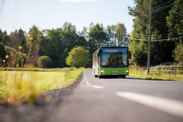 grønn buss kjører ved siden av et jorde