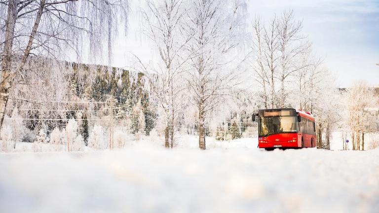 En rød buss ses på avstand i det den kjører gjennom et vinterlandskap