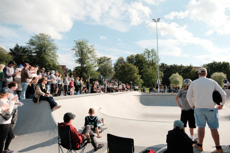 Picture of around 20 people standing in and around a skate park