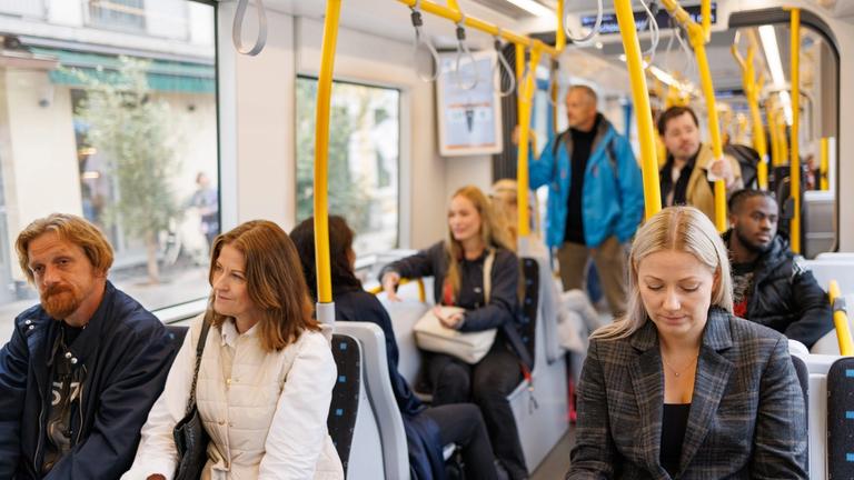 Innsiden av trikken. Mange passasjerer og noen står.