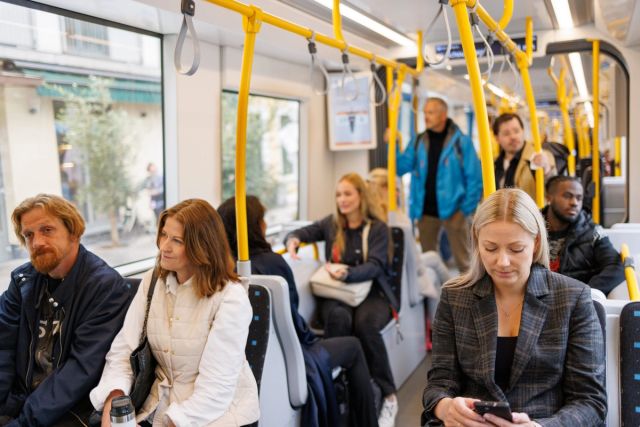 Innsiden av trikken. Mange passasjerer og noen står.