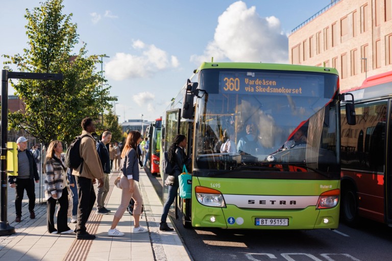 A lot of passengers are waiting to board a green regional bus in the city centre of Oslo