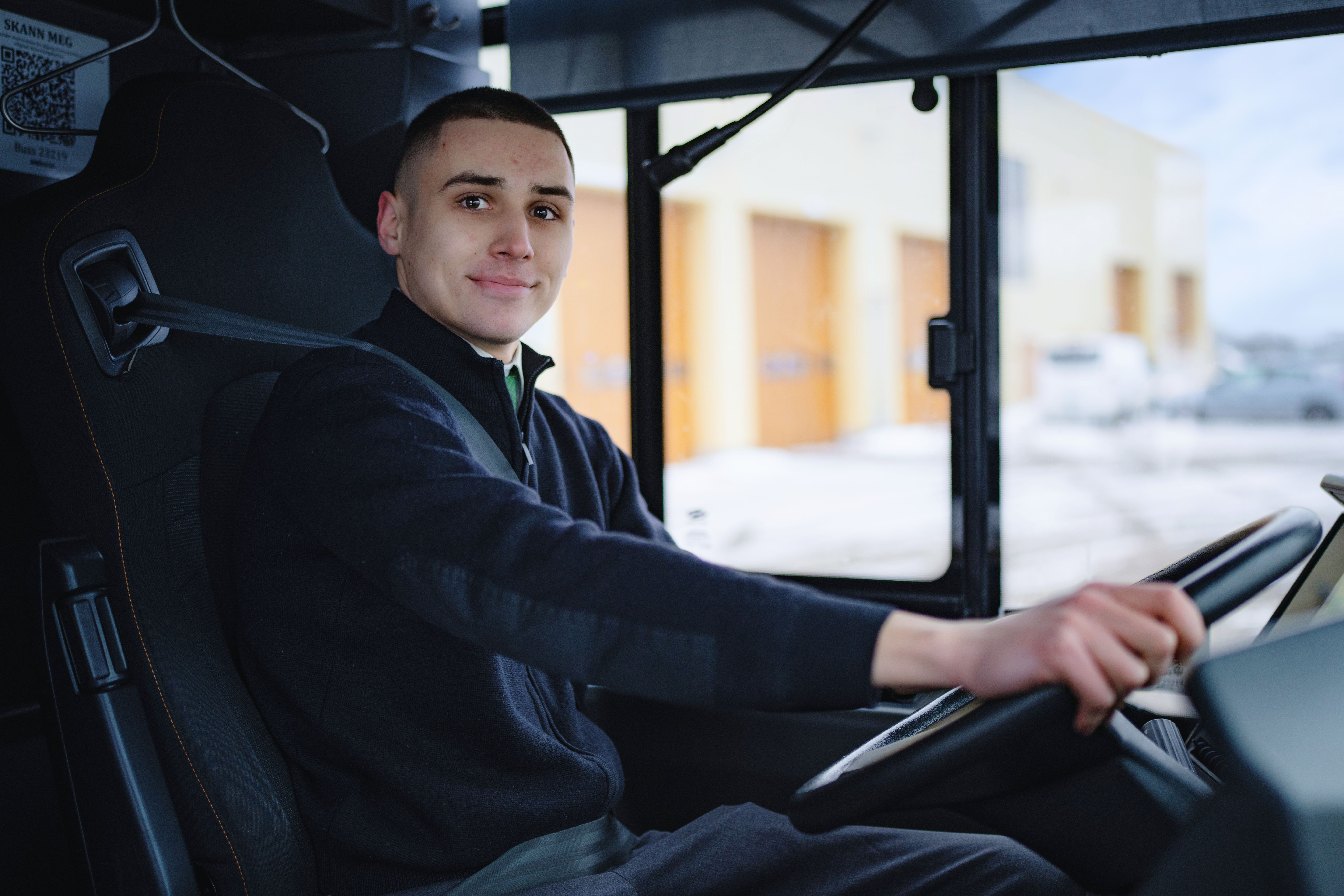 En ung mannlig sjåfør sitter i førersetet til en buss