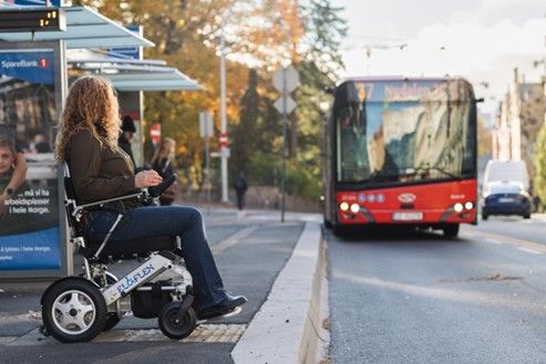 Woman with wheelchair waits for a bus at a bus stop