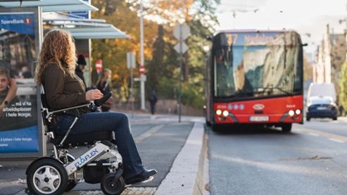 Woman with wheelchair waits for a bus at a bus stop