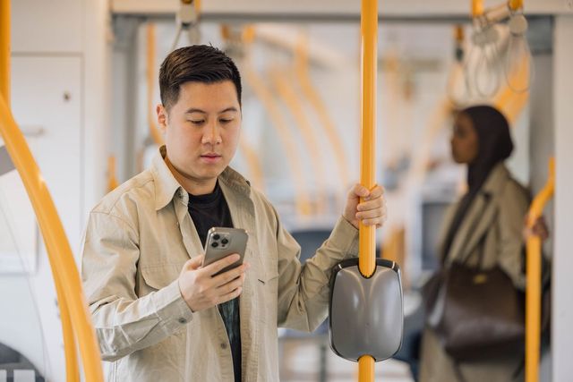 En ung mann holder seg fast på T-banen mens han ser på mobilen