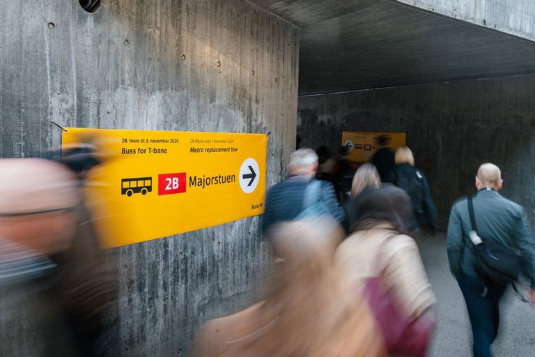 Bilde av mennesker ved en T-banestasjon, med en plakat på veggen med reiseinformasjon
