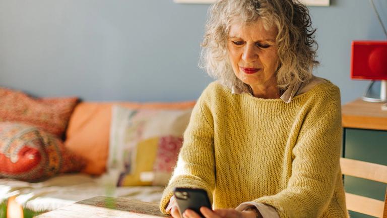 Eldre dame i stuen ser på mobilen