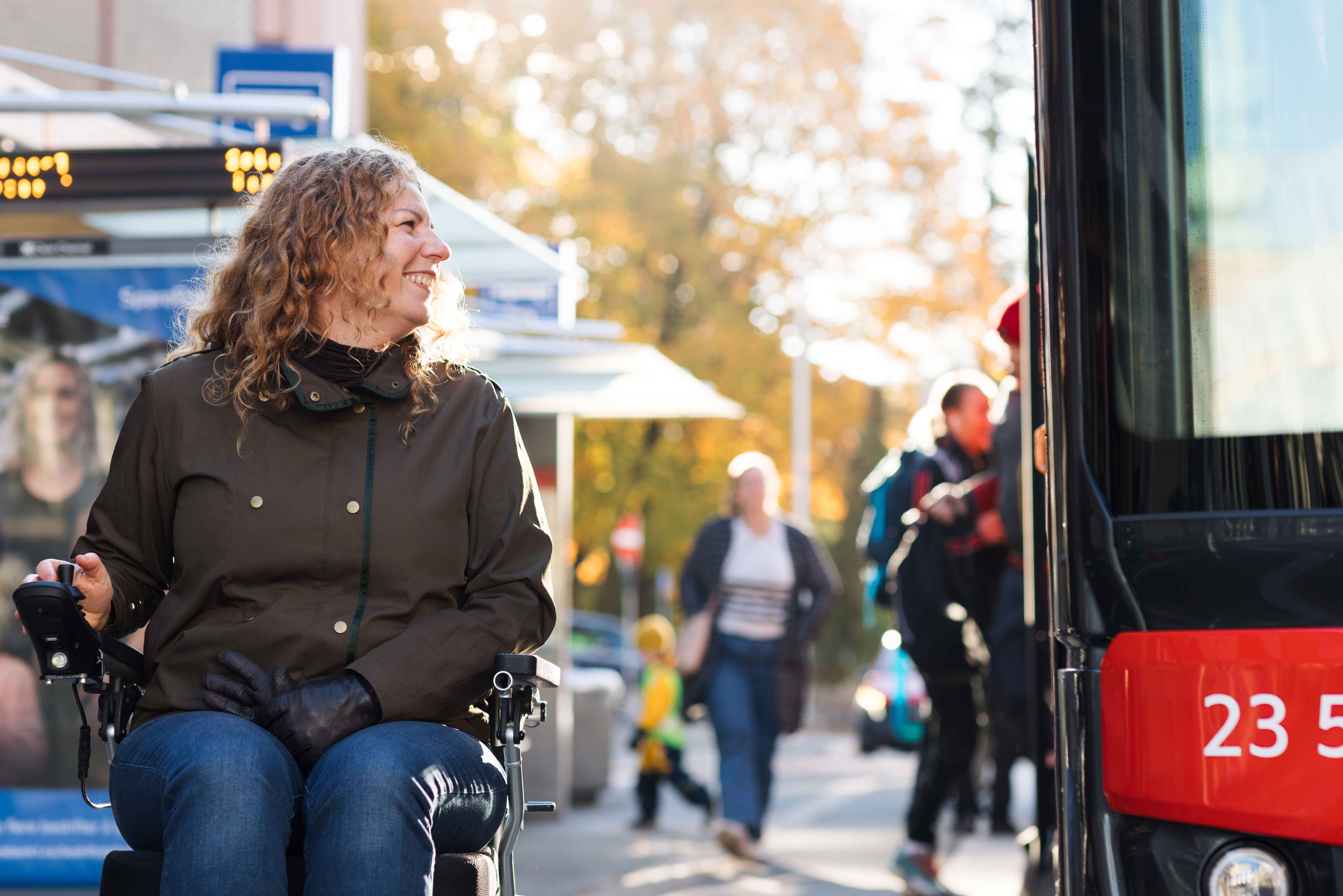 En kvinne i rullestol er på bussholdeplassen når det kommer en buss