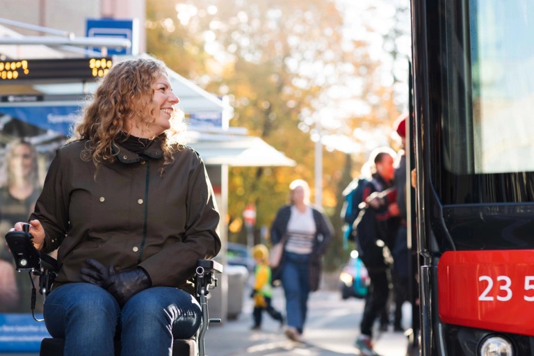 En kvinne i rullestol er på bussholdeplassen når det kommer en buss