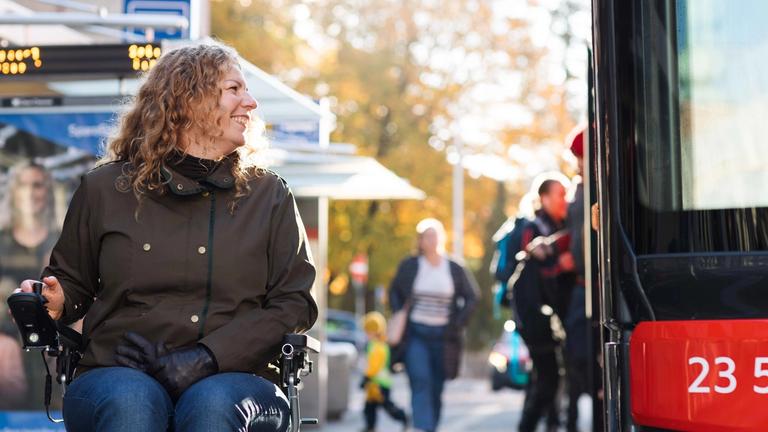 En kvinne i rullestol er på bussholdeplassen når det kommer en buss