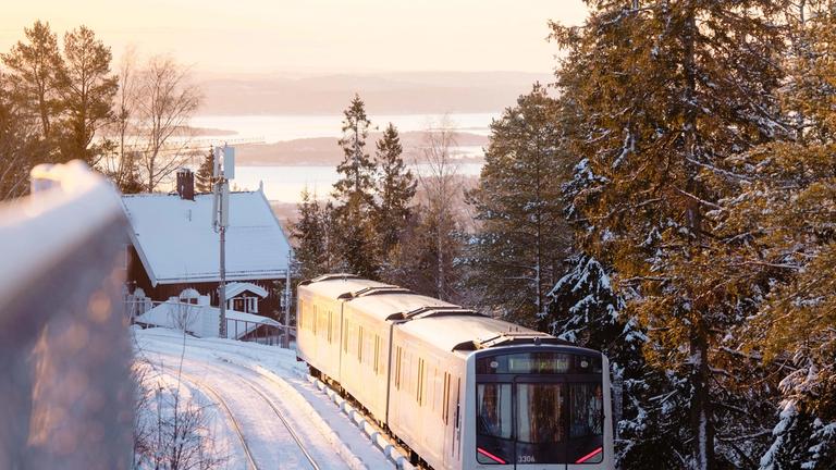 En T-bane i vinterlandskap kjører opp mot Holmenkollen