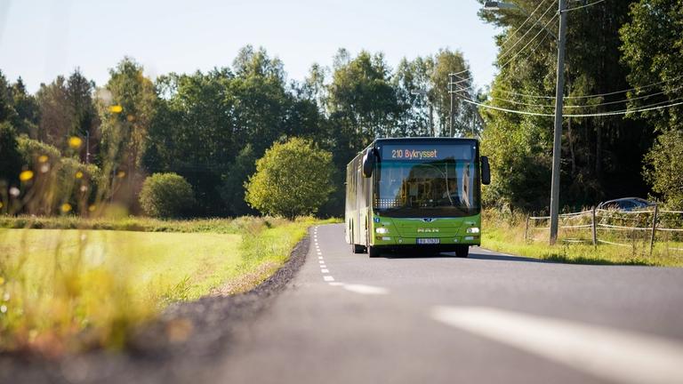grønn buss kjører ved siden av et jorde