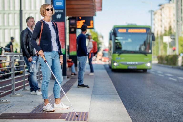 En kvinne med blindestokk på holdeplass