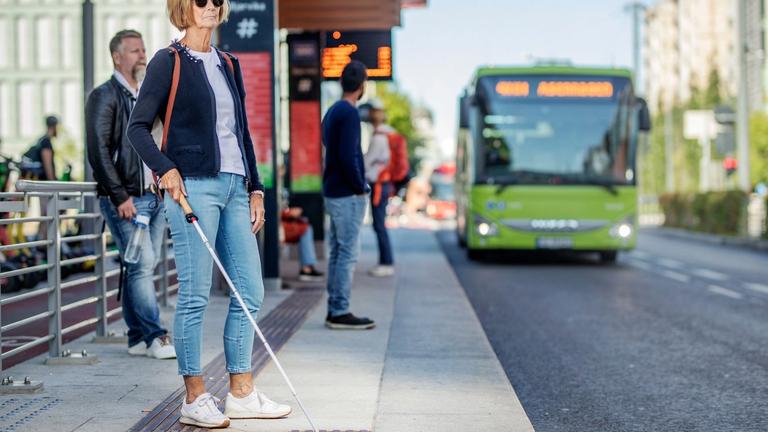 En kvinne med blindestokk på holdeplass