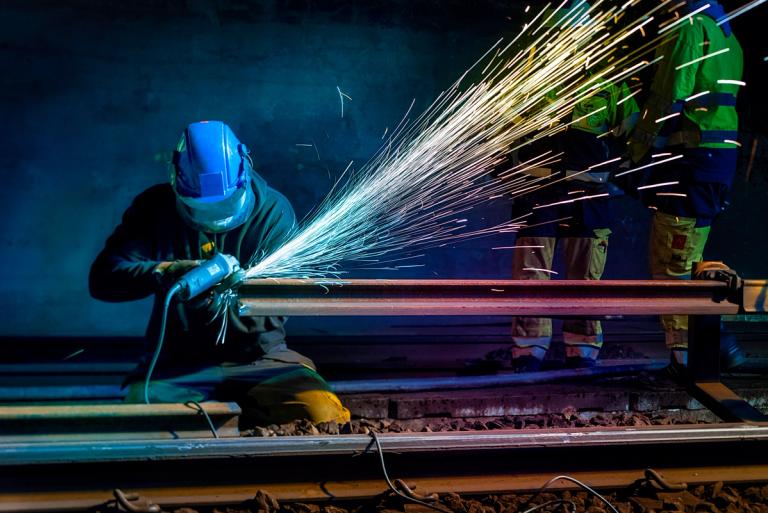Mann med sveisemaske utfører sveisearbeid på en T-baneskinne i tunnel