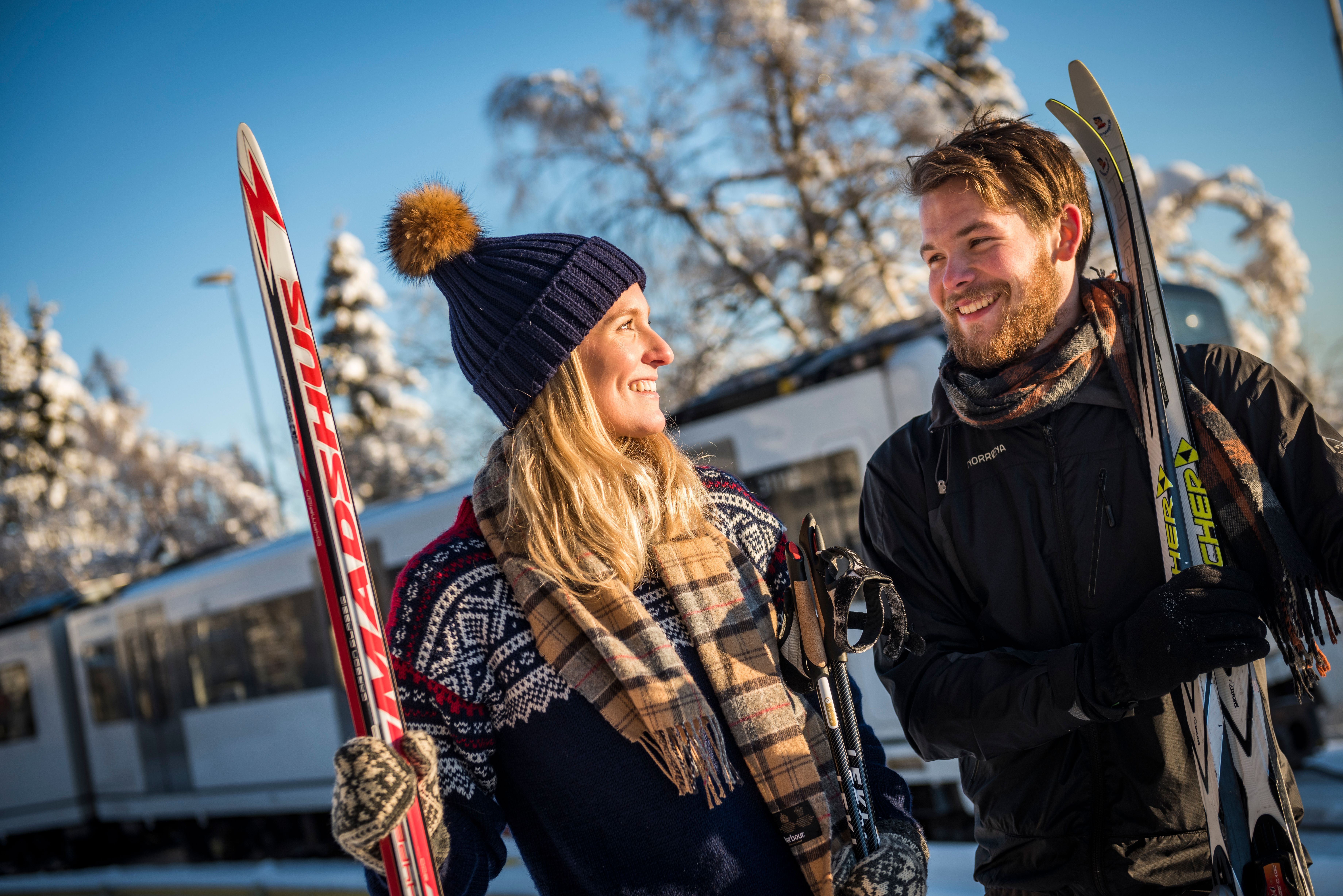 Man and woman with skis in Holmenkollen in sunny weather with the metro in the background