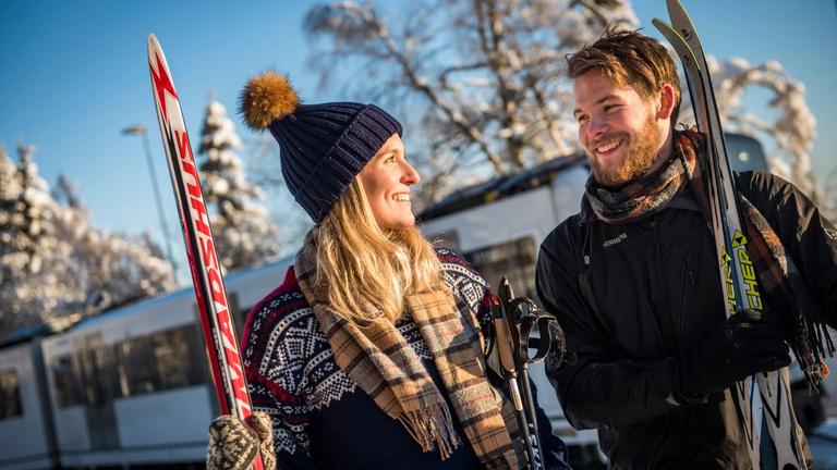 Man and woman with skis in Holmenkollen in sunny weather with the metro in the background