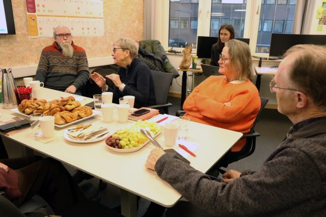 Et møterom med fire pensjonister som sitter rundt et bord og diskuterer
