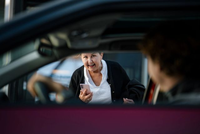 En kvinne kikker inn vinduet til en bilfører mens hun holder en mobil i hånden.