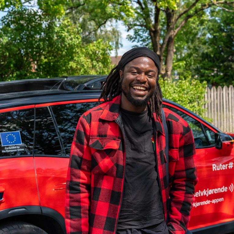 En ung mann står foran en rød, selvkjørende bil