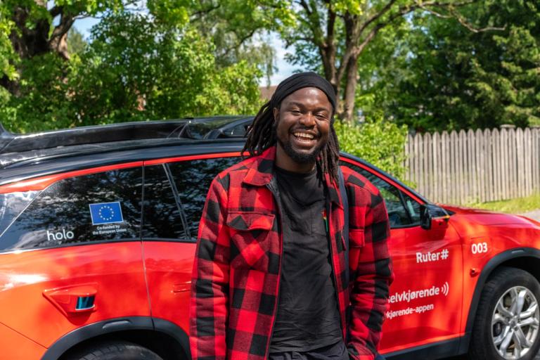 En ung mann står foran en rød, selvkjørende bil