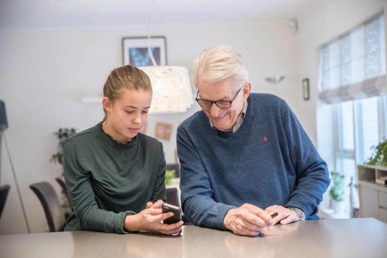En eldre mann og en ung jente ser på Ruter-appen sammen