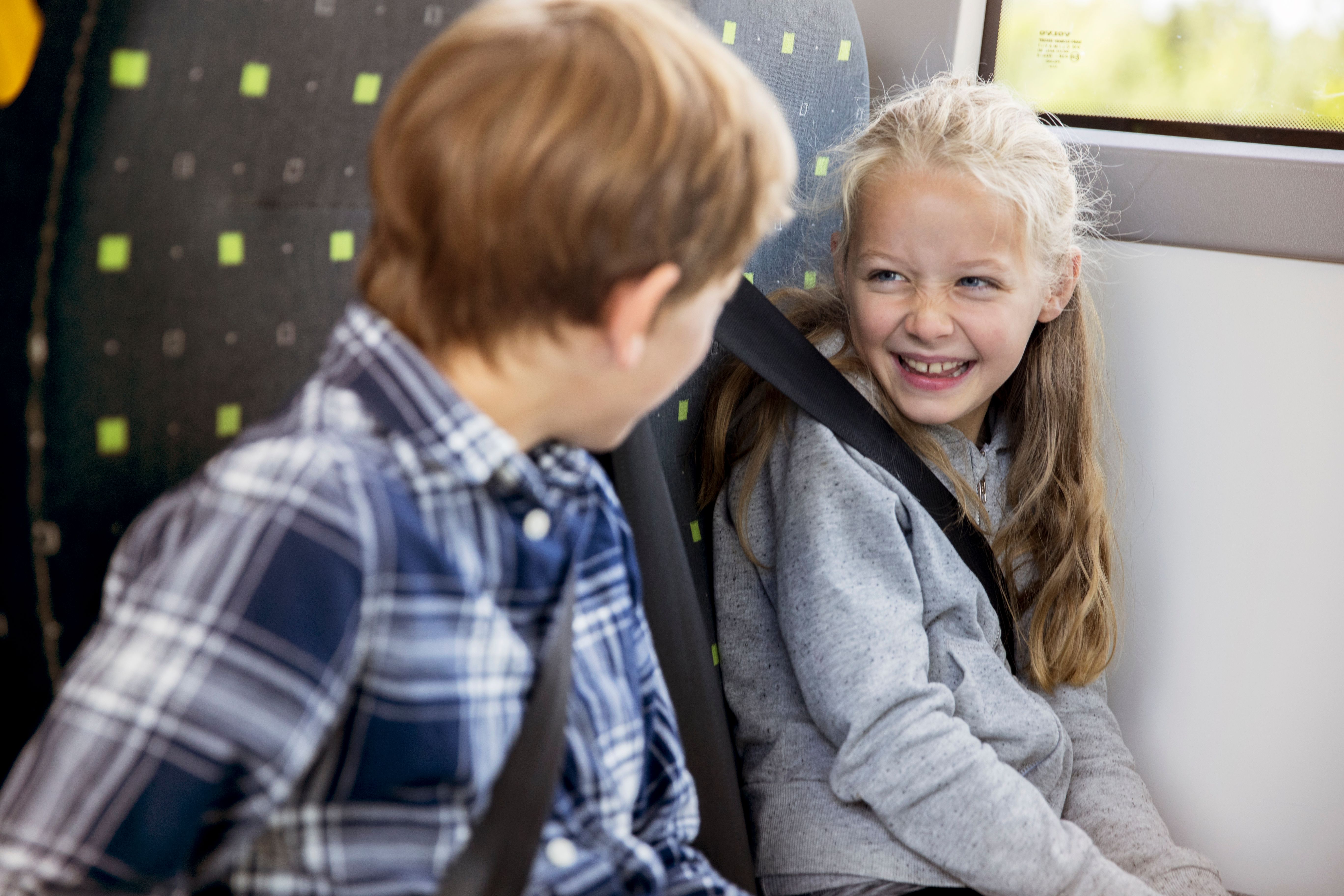 To barn i en skolebuss som ser på hverandre og smiler