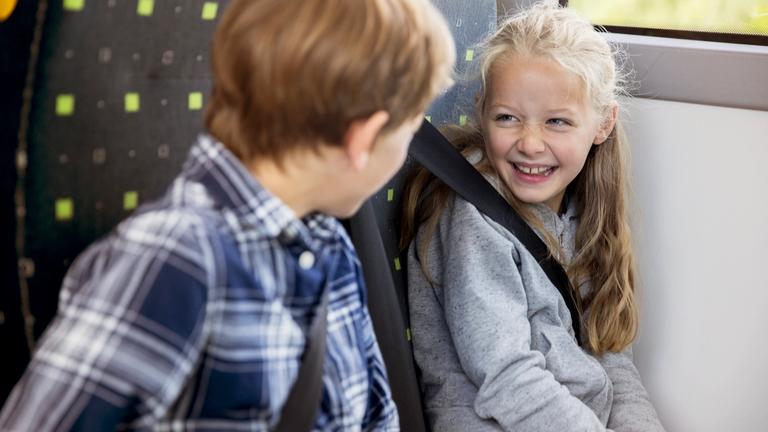 Two children in a schoolbus, sitting next to each other smiling