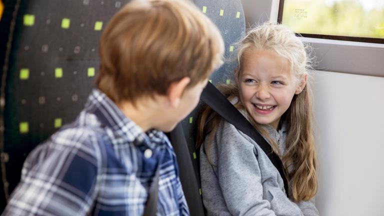 To barn i en skolebuss som ser på hverandre og smiler