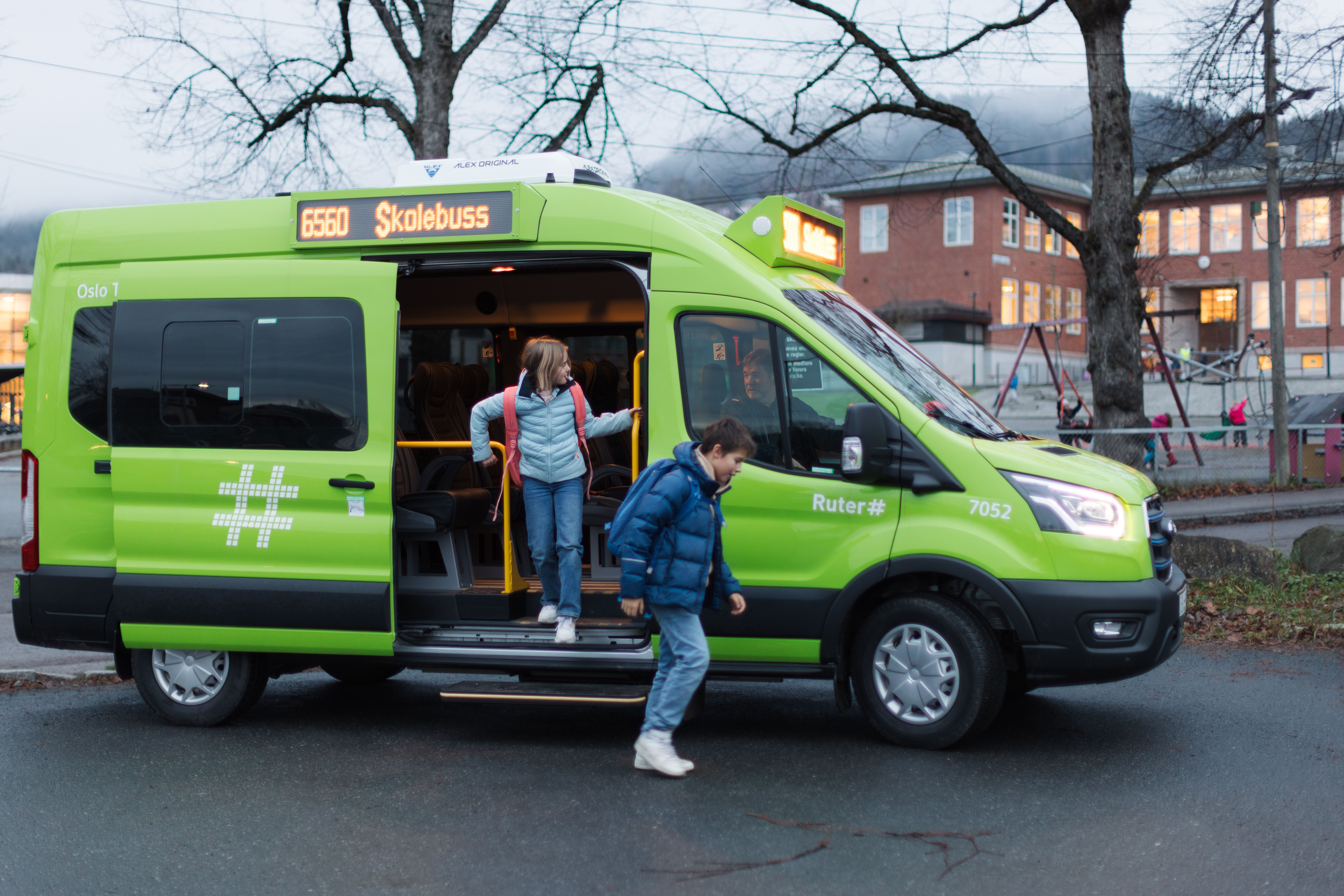 To elever som går ut av grønn minibuss foran en skolen