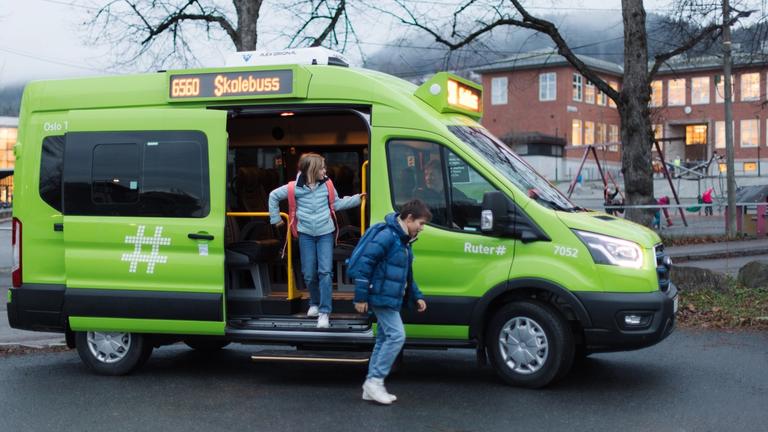 To elever som går ut av grønn minibuss foran en skolen