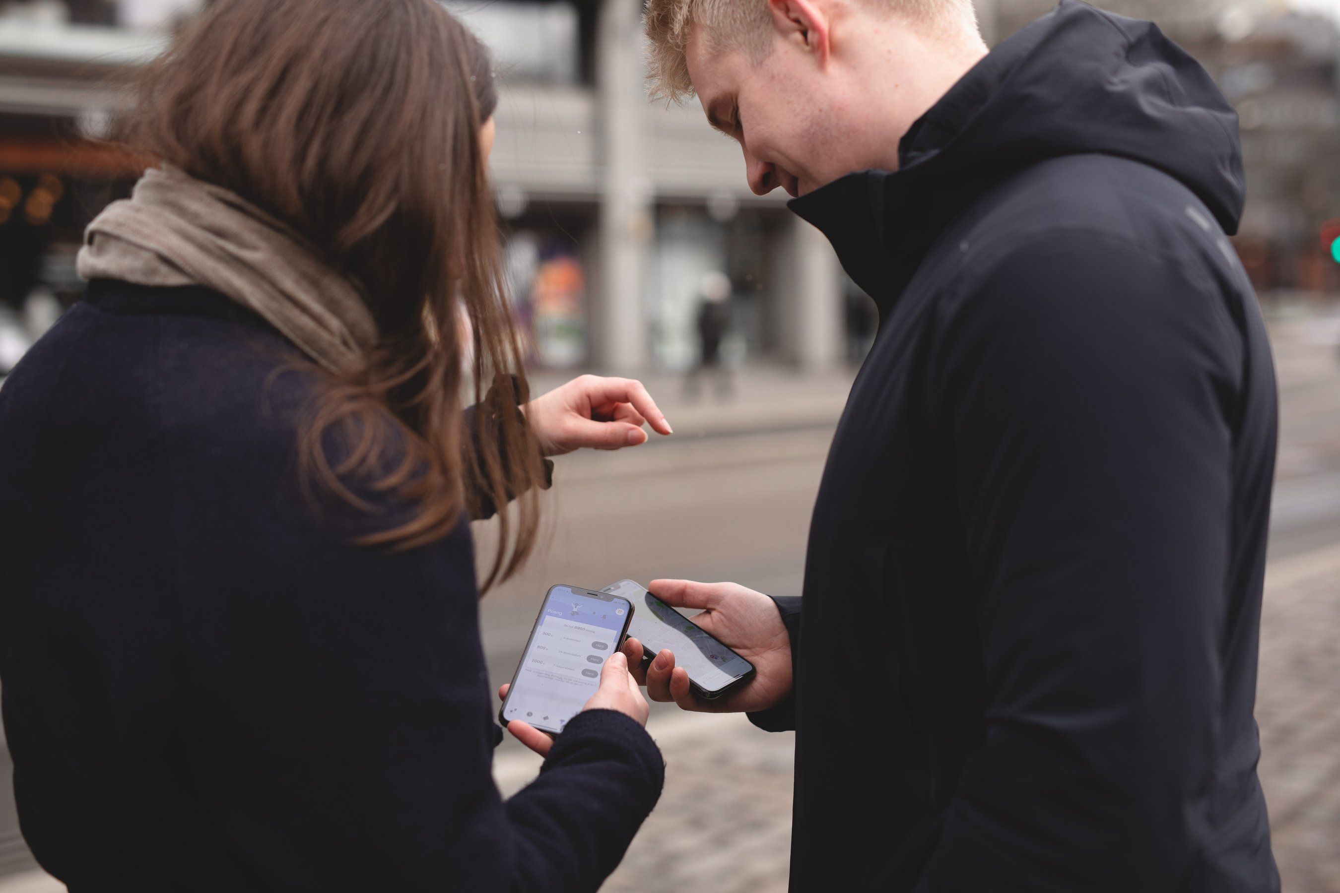 En ung kvinne og en ung mann står ute og holder hver sin mobil med Ruter-appen åpen