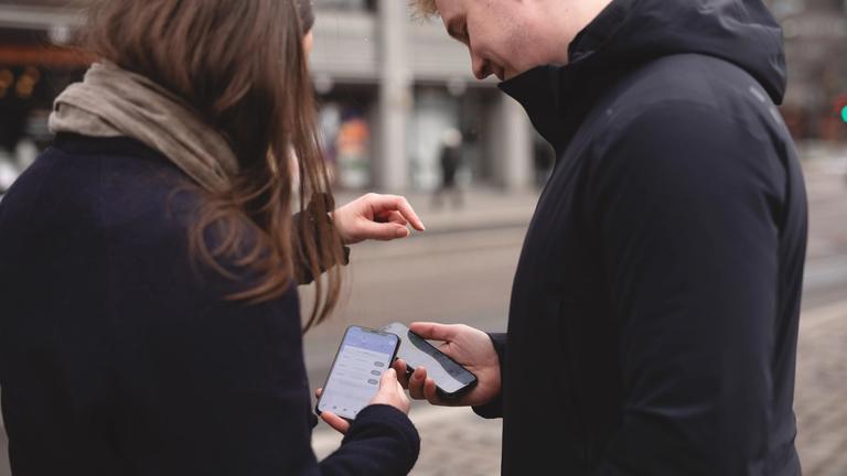 En ung kvinne og en ung mann står ute og holder hver sin mobil med Ruter-appen åpen