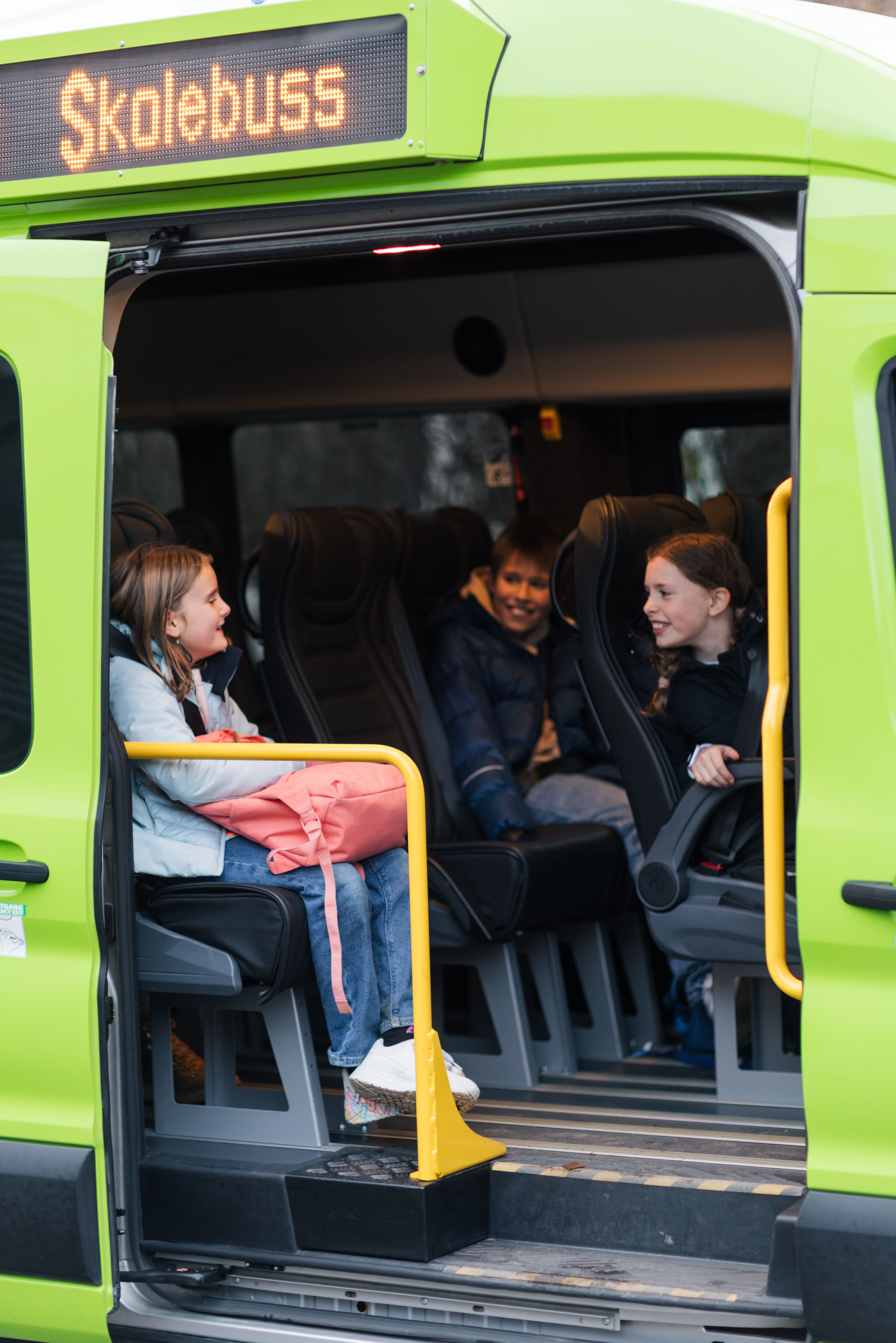 barn sitter i grønn skoleskyss-bil på vei til skolen